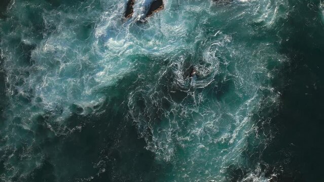 Top down drone shot. Waves wash over sharp rock formations on the coast.