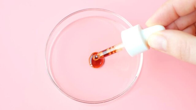 Female hand holds dropper with serum on pink background.