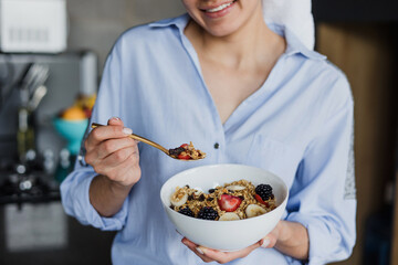 latin young woman in bathrobe eating cereal for breakfast in morning kitchen at home in Mexico,...