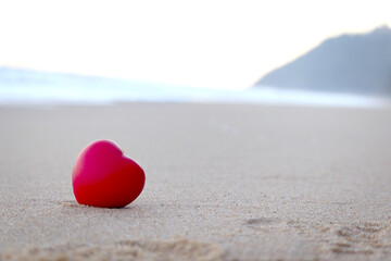 Fototapeta premium Red heart on white sand beach with blured beautiful tropical blue sea, ocean beach nature love concept