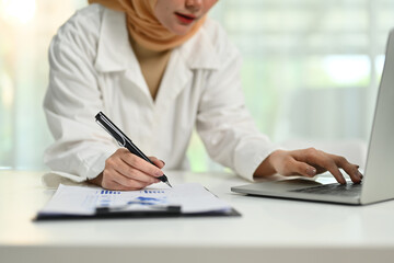 Muslim businesswoman using laptop computer and writing ideas or preparing for negotiations or seminar