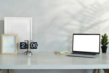 Laptop, vintage flip clock, blank picture frame and houseplant on white table. Copy space for your text