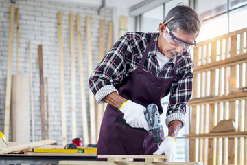 Senior Asian carpenter wear safety glasses and cloth gloves in woodwork workshop, old citizen...