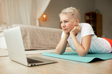 Closeup side view of concentrated fitness female of 50 lying on floor resting chin on hands...