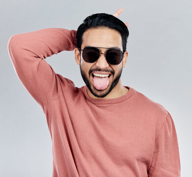 Portrait, tongue out and Asian man with sunglasses, funny and silly against a grey studio background. Face, Japanese male and guy with funky eyewear, shades and comic with humor and goofy expression