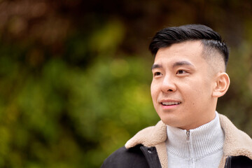 Attractive Asian man looking to the side smiling while relaxing outdoors in a park. 