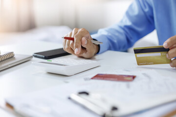 Asian businessman holding credit card to checking invoice and use calculator to calculate cost from...