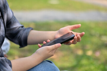 Cropped side view image of a woman in flannel shirt using her phone in the park.