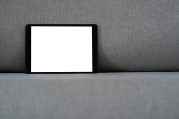 Black tablet computer blank white screen on the modern designed gray fabric sofa.