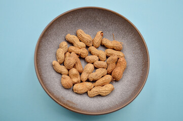A bowl of unshelled dry roasted peanuts against a plain background