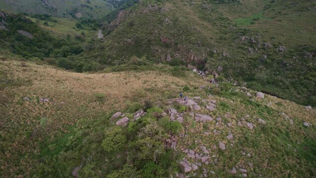 Drone rotates over two friends standing on rocks. On top of a small mountain in a field. Ceballos River. C&oacute;rdoba. Argentina.