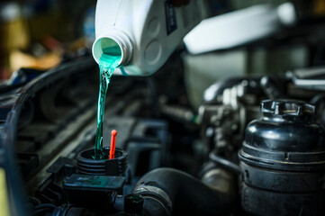 Auto mechanic pouring antifreeze engine coolant into car radiator fill hole.	