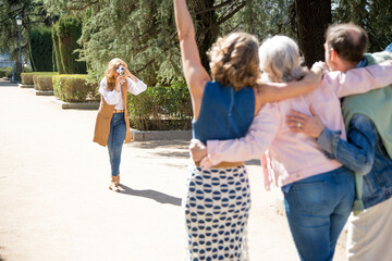 group of middle-aged friends taking pictures of themselves with a camera while posing in the park