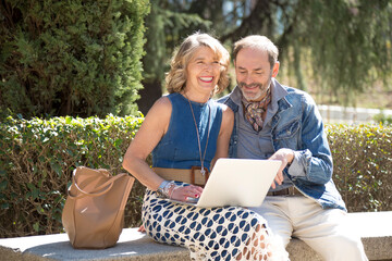 two middle-aged coworkers having a great time while working on their computer in the park