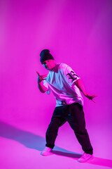 Fototapeta na wymiar Fashion professional handsome breakdancer man with hat in stylish clothes dancing in creative studio with pink and neon lights