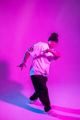Fototapeta na wymiar Handsome young professional dancer dancing in motion in creative studio with neon and pink light