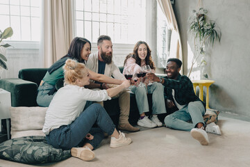 Multiethnic group of happy friends toasting for home aperitif with red wine on sofa