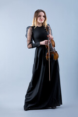 Violinist woman in the evening gown on the grey background.