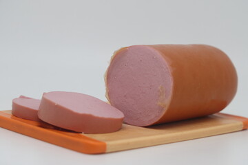 Piece and slices of boiled sausage on cutting board isolated on white background.