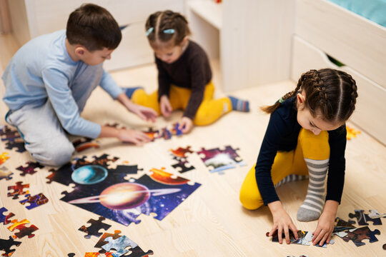 Children connecting jigsaw puzzle pieces in a kids room on floor at home.  Fun family activity leisure.