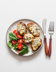 Delicious vegetarian lunch - baked potatoes with gorgonzola and fresh vegetable salad on a light background, top view