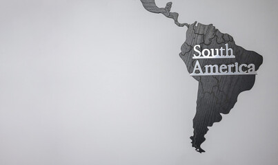 A gray wall with a 3D silhouette of the continent of South America and copy space to the left. A...
