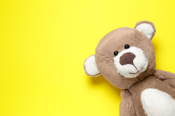 Cute teddy bear on yellow background, top view. Space for text
