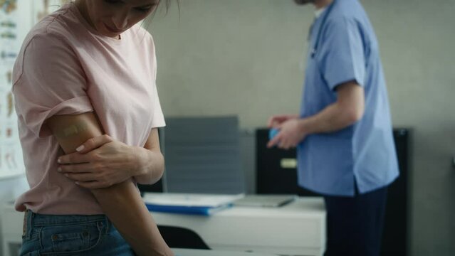 Caucasian female patient with adhesive bandage on her arm just right after vaccination and doctor in the background. Shot with RED helium camera in 8K. 