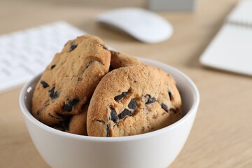 Chocolate chip cookies on wooden table at workplace, closeup