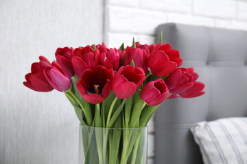 Glass vase with bouquet of beautiful tulips in bedroom