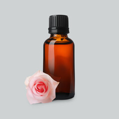 Bottle of rose essential oil and flower on light grey background