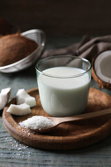 Glass of delicious coconut milk, spoon with flakes and nuts on wooden table