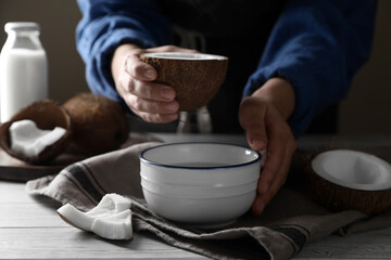 Woman holding nut with coconut milk at white wooden table, closeup
