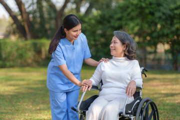 Fototapeta premium Asian nurse takes a patient in a wheelchair to make her feel refreshed and relaxed at the park.