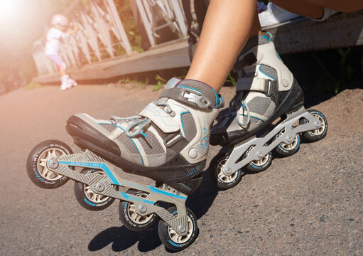 Close up girl putting on inline skates rollers preparing in public park in summer. Teenager leisure outdoor sport activity game.