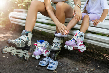 Mother and daughter taking off inline roller on bench after skating in public park together. Family leisure sport activity weekend. Copy negative space