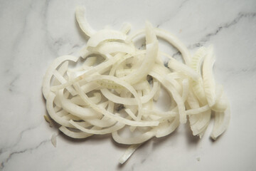 Half rings sliced onions on white marble background. Photo show how does onion sliced into half ring or half moon slices look like