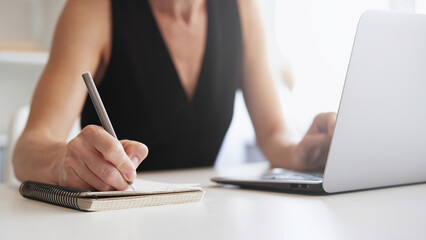 Fototapeta premium Online e-learning. Internet research. Distance education. Unrecognizable female student watching video lesson on laptop taking notes at light workplace.
