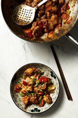 Chicken Manchurian in plate near wok where chicken was fried and cooked with sauce. Top view