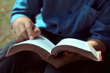 Close-up of Christian man's hands while reading the Bible outside.Sunday readings, Bible education. spirituality and religion concept. Reading a book.The books of the Bible, Concepts of Christianity.