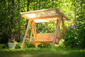 Wooden garden swing in summer on green grass.Rest on a country plot. Wooden furniture for the...