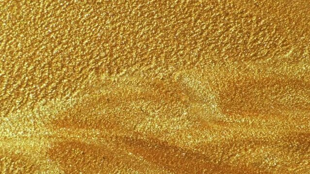 Gold ink. Paint flow. Sand texture. Defocused sparkling metallic yellow color liquid wave motion abstract background with free space.