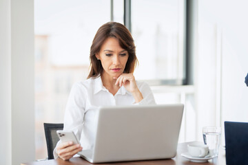 Portrait of confident business woman wearing white shirt and using laptop while working at the...