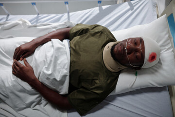 High angle view of African American soldier lying on bed with wound in military hospital