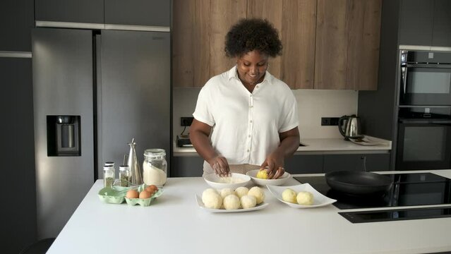 Happy young cuban woman breading mashed potatoes balls while dancing to prepare cuban style stuffed potatoes.