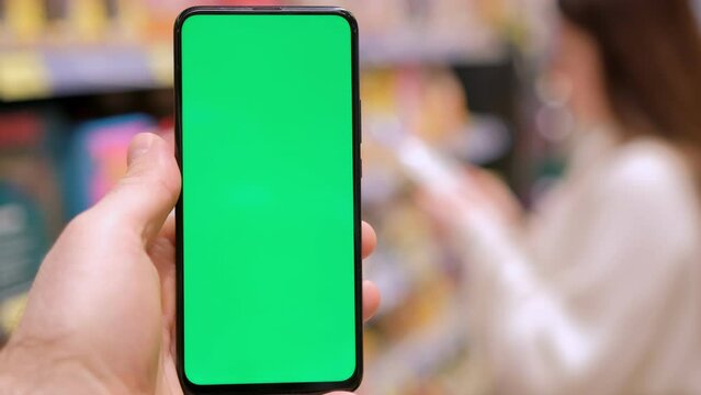 4k Mobile phone Chroma key for mobile app application. Close up of man hand holds smart phone with green screen at shopping mall store. Buying food at supermarket, grocery shop center online. Gadgets