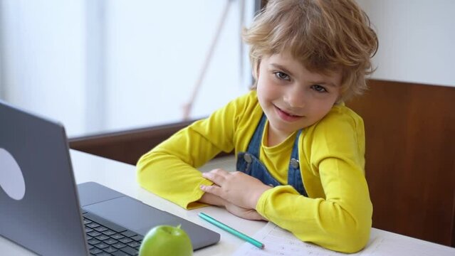 Cute Schoolboy child eating apple while using laptop online educational lesson course at home. Distance learning course remote video conference. Schoolgirl study does school homework.