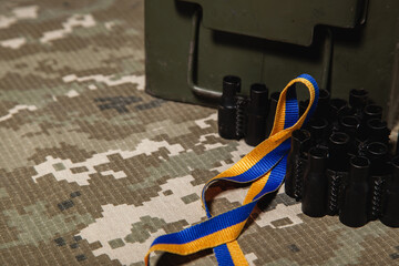 Fototapeta premium Military green box, machine gun ribbon and blue-yellow ribbon, colors of the Ukrainian flag, on the background of the green military pixel.