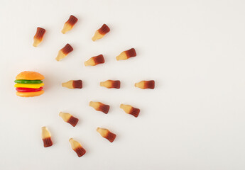 Gummy candies in burger and bottles shape arranged in line on white background. Food compatibility concept.