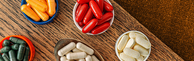 pills banner top view. multivitamin dietary supplements on a wooden desk. mental wellbeing and personal health concept - obrazy, fototapety, plakaty